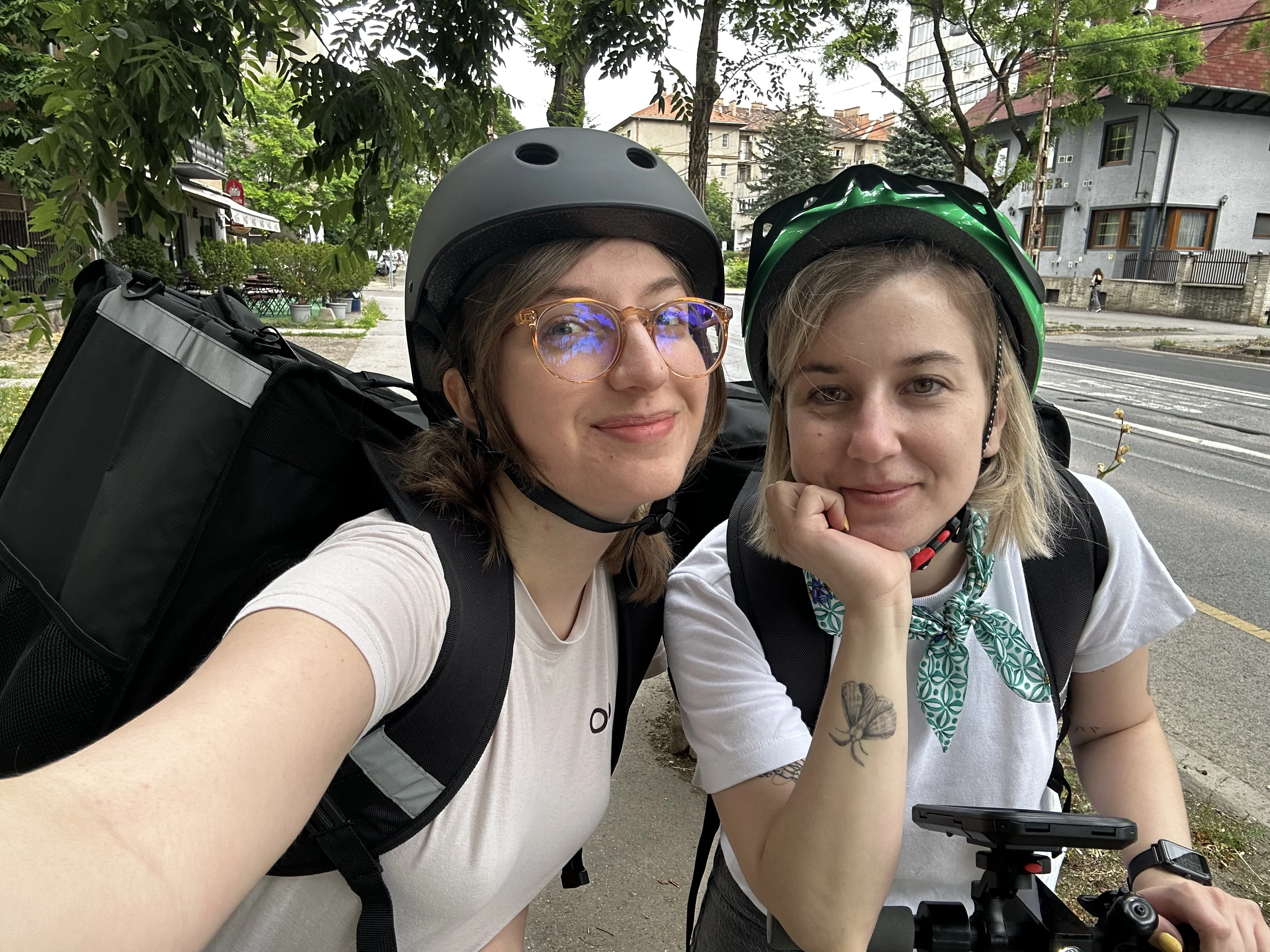 Two Boolanga team members wearing helmets and delivery bags, smiling for a selfie on their bikes